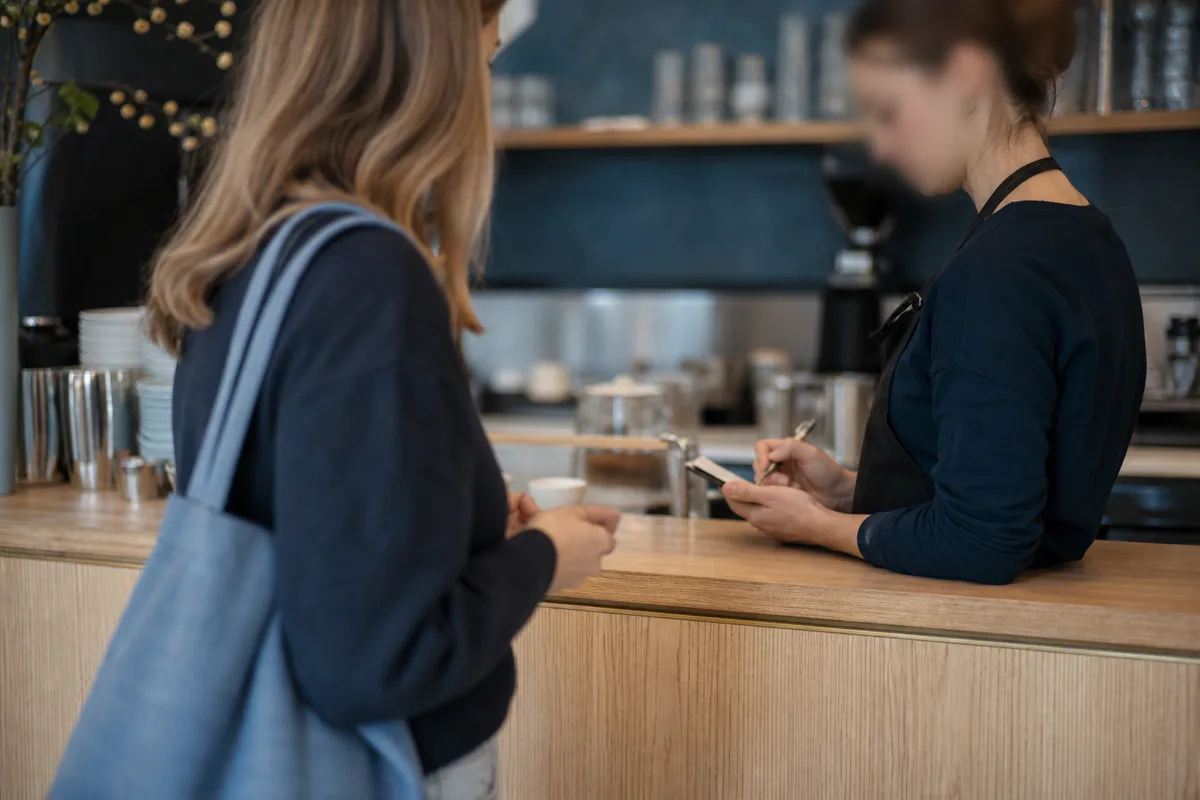 Un client commande poliment au comptoir d&rsquo;un café allemand, la serveuse note sur son carnet
