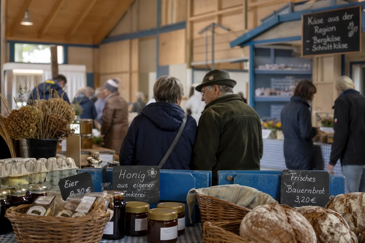 Un marché de village en Bavière avec des panneaux manuscrits en allemand et des habitants en discussion